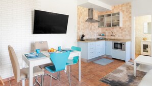 Une cuisine compacte avec un crédence carrelée, un four à micro-ondes encastré et un petit coin repas comprenant une table et des chaises.