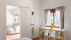 Une chambre avec un lit, une armoire blanche, une console sur laquelle sont posées des bougies, et une vue sur un balcon.