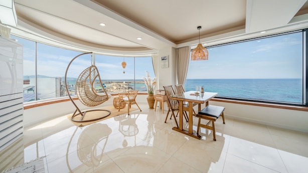 A modern dining area with a view of the sea, a hanging chair, and a table with chairs. - Donghae Il Mare Pension (Donghae)