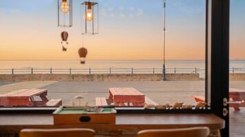 A beachside view from a window overlooking a wooden pier with benches and tables, and a clear view of the ocean.