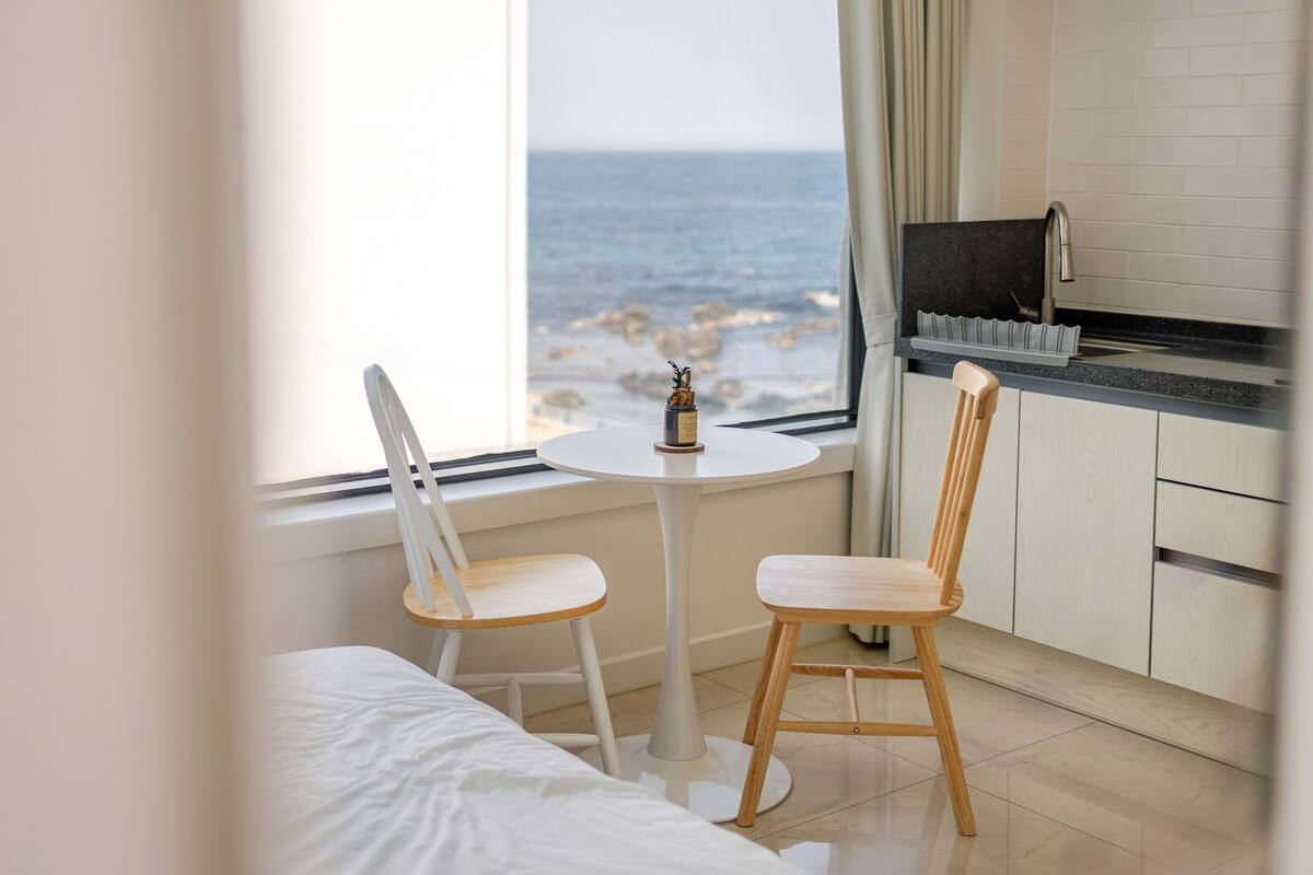 Een moderne kamer met een bed, een klein rond tafeltje, twee houten stoelen, een televisie en uitzicht op zee.