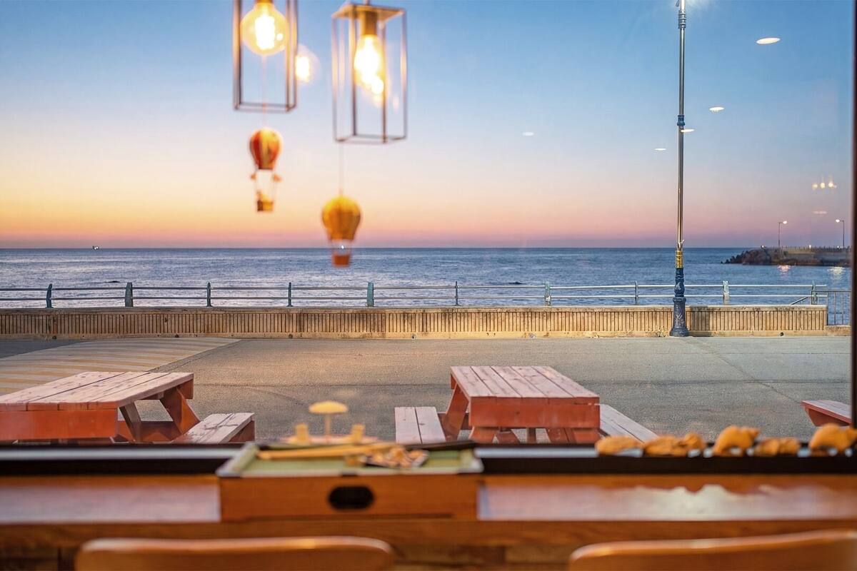 Uitzicht op zee vanaf een restaurant met houten tafels en hangende lampen.