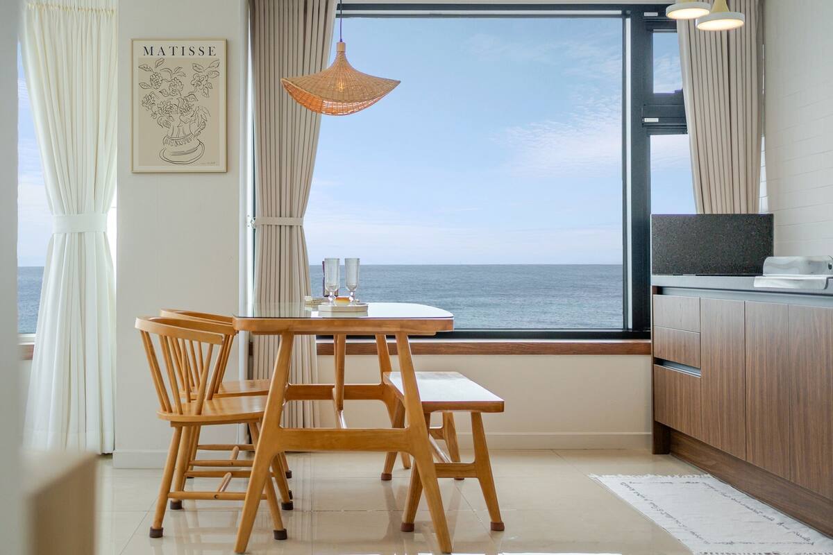 Een eetgedeelte met uitzicht op zee, een tafel met stoelen, een hanglamp en een keukentoog.
