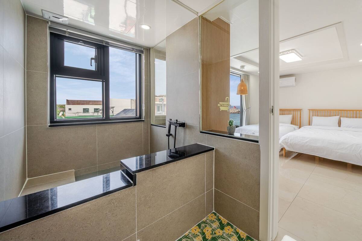 Een moderne hotelkamer met een groot raam, een badkamer met douche en een bed met wit beddengoed.