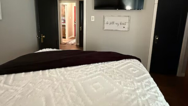 A bedroom with a bed, a television mounted on the wall, and a door leading to another room. - Riverside Lodge (Clarendon)