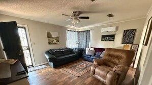 A living room with a ceiling fan, a black leather sofa, a brown leather armchair, a patterned rug, and a blue couch. - Riverside Lodge (Clarendon)