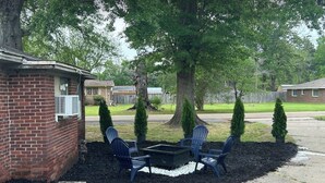 A brick building with a small patio area, outdoor seating, and a large tree. - Riverside Lodge (Clarendon)