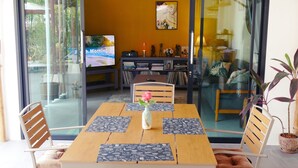 Een eethoek met een tafel voor vier personen, een televisie op de achtergrond en een boekenkast met boeken en decoratieve objecten.