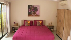 Een slaapkamer met een groot bed, een plafondventilator, een schilderij aan de muur en een kledingkast.