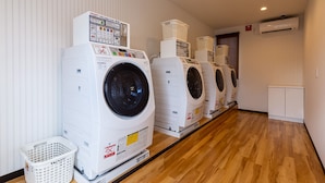 A row of stacked front-loading washing machines in a laundry room with wooden flooring and white walls. - HOTEL R9 The Yard Mokaaramachi (Mooka)