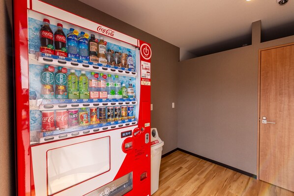 A vending machine with various beverages, including Coca-Cola and Fanta, in a room with wooden flooring and a door. - HOTEL R9 The Yard Mokaaramachi (Mooka)