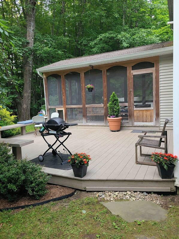 A covered outdoor deck with a grill, potted plants, and a bench.