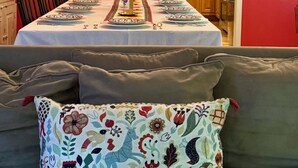 Un comedor con una mesa preparada para cuatro personas, una araña, una pared roja y una cocina visible a través de un umbral abierto.