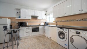 Une cuisine compacte avec des meubles blancs, un four encastré, un four à micro-ondes, un lave-linge et un coin repas équipé de tabourets.