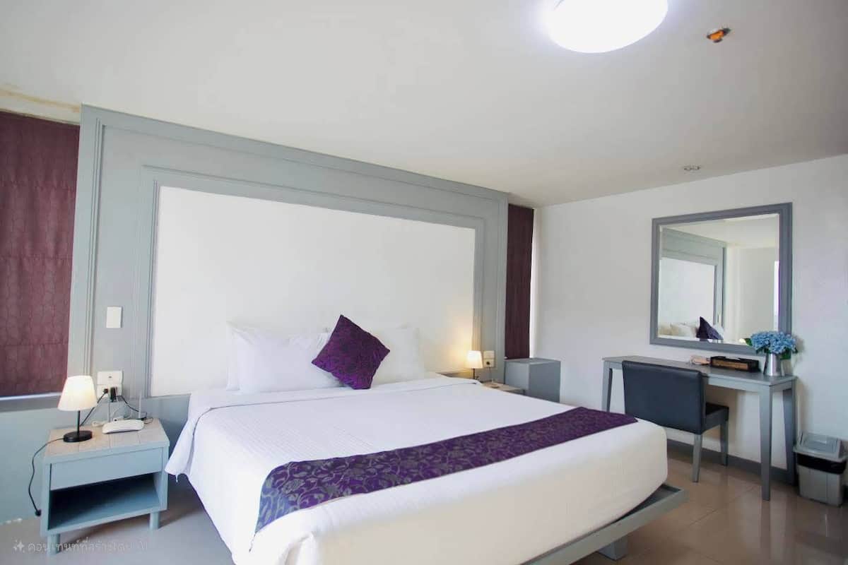 Ein Hotelzimmer mit einem großen Bett, einem Schreibtisch, einem Spiegel und einem Nachttisch mit einer Lampe.