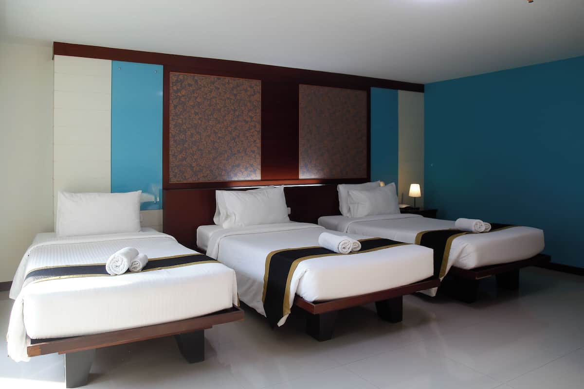 Ein Hotelzimmer mit drei Einzelbetten, einem Holzkopfstück und einer großen Wandverkleidung.