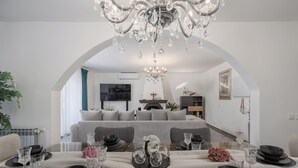 A dining area with a table set for four, a chandelier, and a sofa in the background.