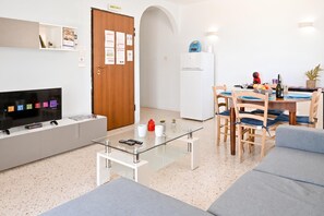 A modern living room with a flat-screen TV, a glass coffee table, and a seating area with a sofa and chairs.