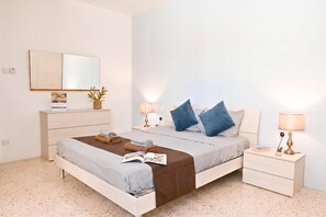 A bedroom with a bed, bedside tables, a dresser, a mirror, and a wall-mounted lamp.