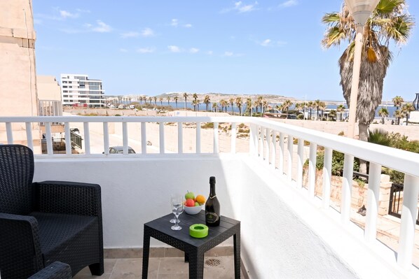 A balcony with a view of the sea, a table with a bottle and fruit, and a chair.