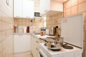 Cocina compacta con armarios blancos, microondas, estufa y refrigerador.