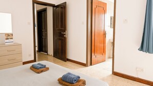 A hotel room with a bed, a wooden door, a bathroom visible through an open door, and a blue curtain.