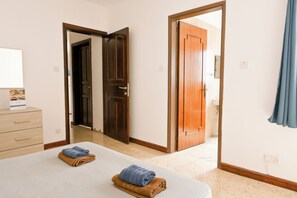 A hotel room with a bed, a wooden door, a bathroom visible through an open door, and a blue curtain.