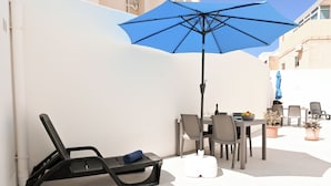 A patio with a table, chairs, a blue umbrella, and a lounge chair.