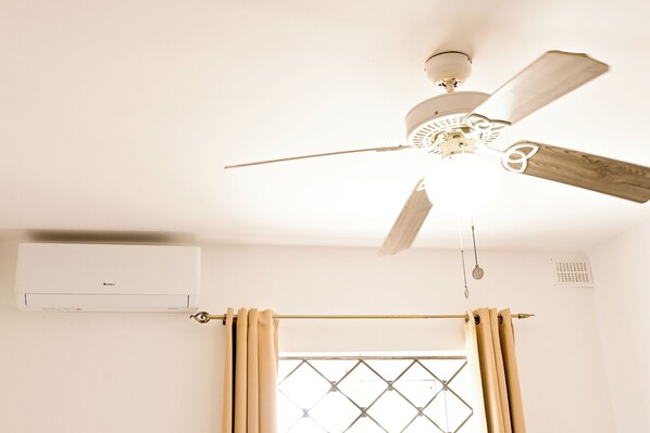 A ceiling fan with wooden blades, a window with a diamond-patterned grille, and an air conditioning unit on the wall.