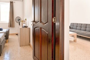 A room with a wooden door, a bed, a sofa, a small table, and a floor lamp.