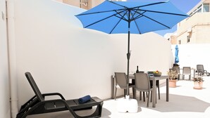 A patio with a table, chairs, a blue umbrella, and a lounge chair.