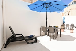 A patio with a table, chairs, a blue umbrella, and a lounge chair.