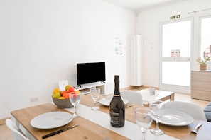 Un área de comedor con una mesa dispuesta para dos, una botella de vino y un bol de fruta.