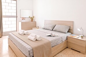 Un dormitorio moderno con cama, mesitas de noche, lámpara y ventana con vista a un muro de ladrillo.