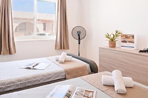 Habitación de hotel con dos camas, un ventilador, un aparador y una ventana con cortinas.