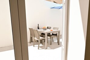 A dining area with a table and chairs, a bottle of wine, and a bowl of fruit.