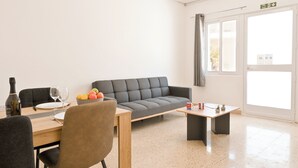 Una sala de estar moderna con un sofá, una mesa de comedor con sillas, una mesa de centro y una ventana con cortinas.