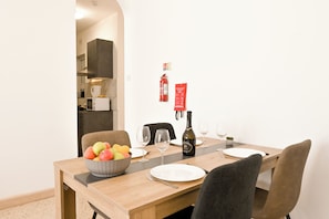 A dining area with a wooden table, chairs, a bowl of fruit, wine glasses, and a fire extinguisher on the wall.