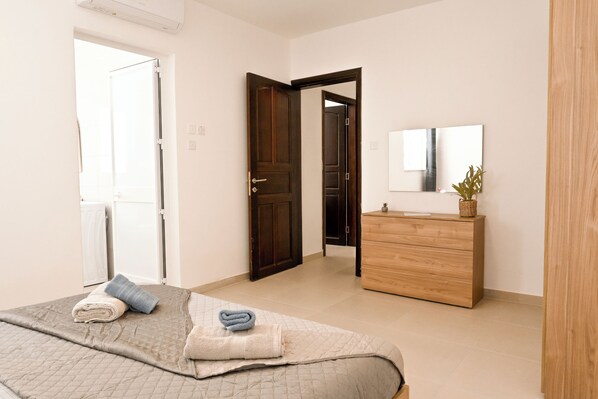 A bedroom with a bed, a wooden dresser, a mirror, and a door leading to another room.