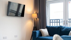 Una sala de estar moderna con un sofá azul, una lámpara de pie y un televisor de pantalla plana montado en la pared.