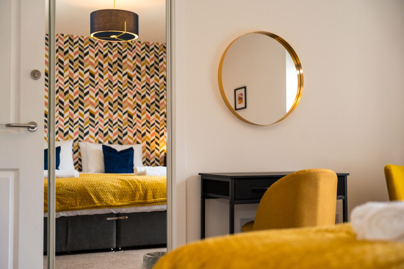 A hotel room with a bed, a desk, a chair, and a mirror on the wall.