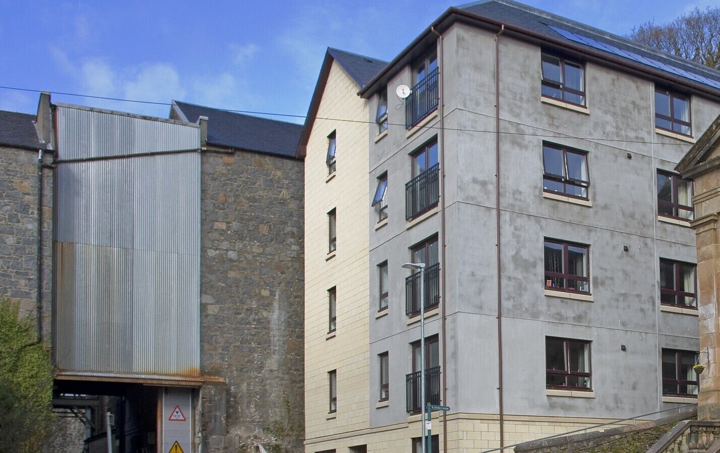 Un immeuble à plusieurs étages, dont la façade combine des matériaux en pierre et des matériaux modernes, agrémenté de balcons et doté d’une entrée bien visible, sur laquelle est apposé un panneau d’avertissement.