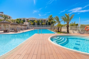 A swimming pool with lounge chairs and umbrellas, surrounded by palm trees and a clear blue sky.