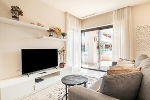 A modern living room with a flat-screen TV, a sofa, a coffee table, and a balcony with a view.