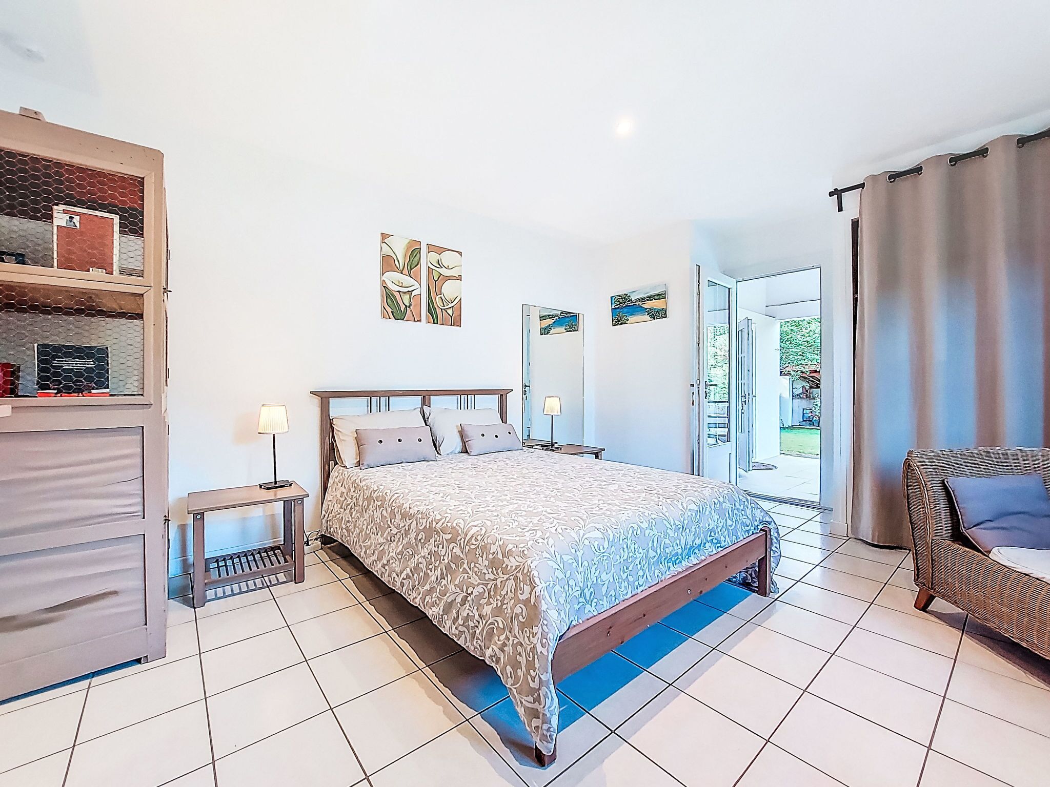 Une chambre à coucher comprenant un lit, des tables de chevet, une armoire et donnant sur l’extérieur.