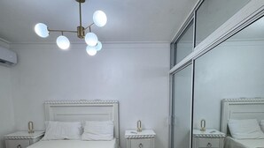 Quarto com um espelho grande, uma cama com cabeceira branca, duas mesas de cabeceira com luminárias e um lustre.