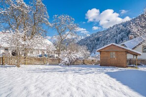 Paisatge cobert de neu amb una cabana de fusta i una casa al fons.