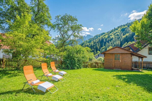 Un espace verdoyant avec quatre chaises longues, un chalet en bois et une chaîne de montagnes en arrière-plan.
