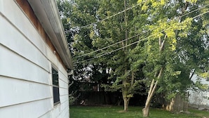 A concrete patio adjacent to a white house with a wooden fence and trees in the background. - Point peele (Leamington)