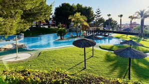 Una piscina con un puente, rodeada de palmeras y un césped cuidado.